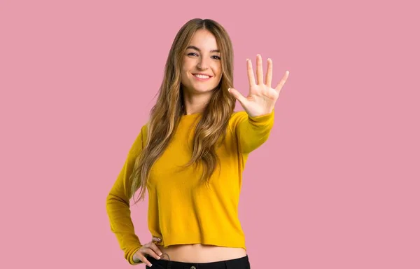 年轻的女孩与黄色毛衣计数五与手指在被隔绝的粉红色背景 — 图库照片