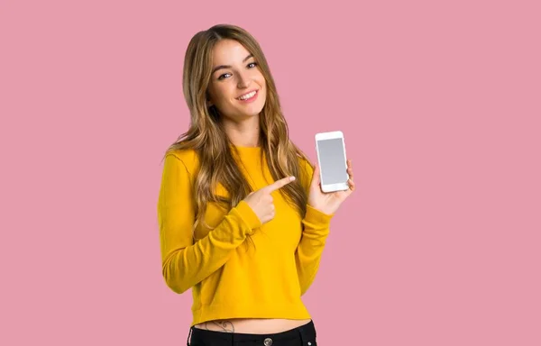 Fiatal Lány Mutatja Mobil Elszigetelt Rózsaszín Háttér Sárga Pulóver — Stock Fotó