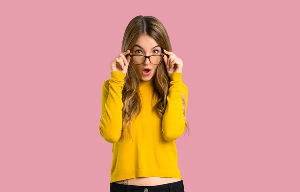 メガネと分離のピンクの背景に驚かれる黄色いセーターを着ての少女 — ストック写真