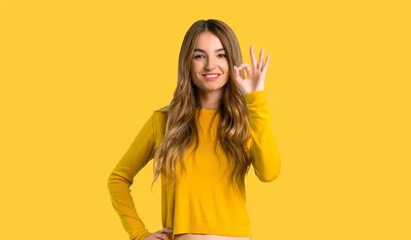 Молода Дівчина Жовтим Светром Показує Знак Пальцями Ізольованому Жовтому Фоні — стокове фото
