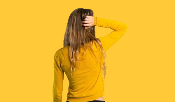 young girl with yellow sweater on back position looking back while scratching head on isolated yellow background