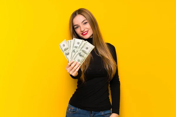 たくさんのお金を取って 黄色の背景で若いきれいな女性 — ストック写真