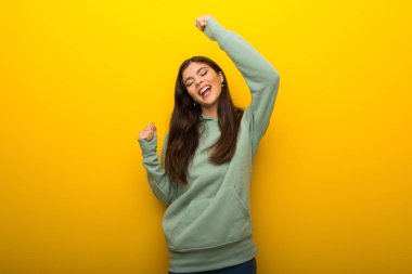 Teenager girl with green sweatshirt on yellow background celebrating a victory clipart