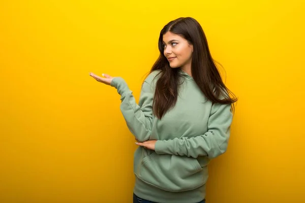 Teenager Mädchen Mit Grünem Sweatshirt Auf Gelbem Hintergrund Hält Kopierraum — Stockfoto