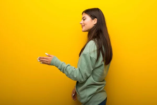少女与绿色运动衫在黄色背景握手后好交易 — 图库照片