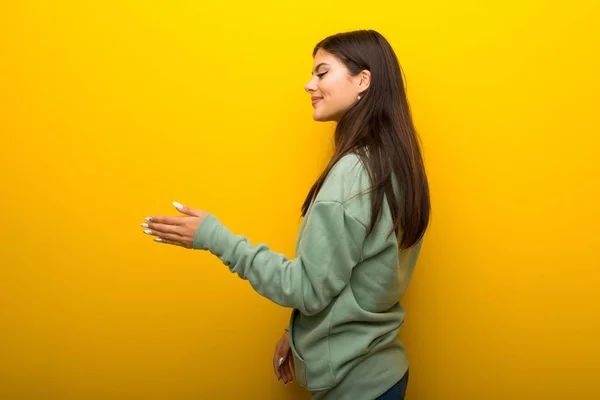 Adolescente Chica Con Sudadera Verde Sobre Fondo Amarillo Apretón Manos —  Fotos de Stock