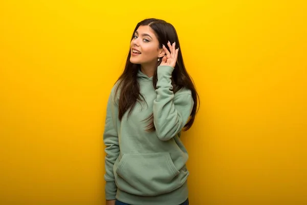 Chica Adolescente Con Sudadera Verde Sobre Fondo Amarillo Escuchando Algo —  Fotos de Stock