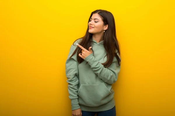 Chica Adolescente Con Sudadera Verde Sobre Fondo Amarillo Apuntando Hacia —  Fotos de Stock