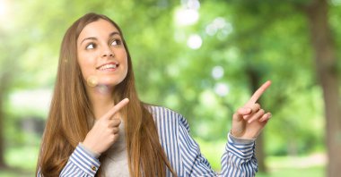 İşaret parmağı ile işaret ve açık havada ararken çizgili gömlek ile genç kız