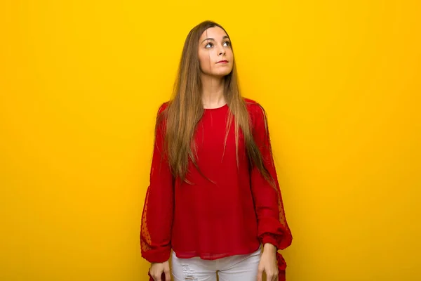Młoda Dziewczyna Czerwoną Sukienkę Żółtej Ścianie Patrząc Poważną Twarz — Zdjęcie stockowe