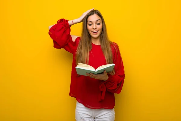年轻的女孩与红色礼服在黄色的墙壁上惊讶 一边享受看书 — 图库照片