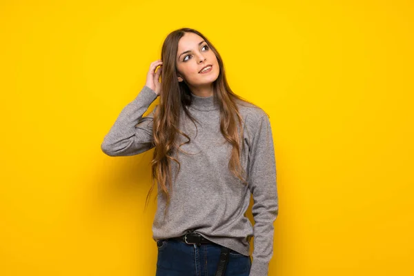 Young woman over yellow wall thinking an idea while scratching head