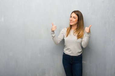 Genç kadın hareketi her iki el ile Yaşasın vererek ve gülümseyen dokulu duvar