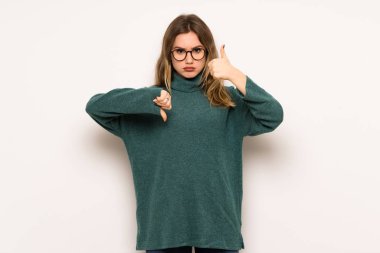 Genç kız iyi-kötü işaret yapma beyaz duvar yüzünden. Arasında kararsız Evet ya da değil