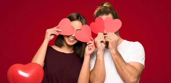 バレンタインの赤い背景の上の心のシンボルを保持のカップル — ストック写真