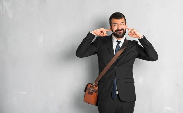 Businessman with beard covering both ears with hands