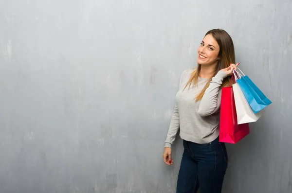 Young woman on textured wall holding a lot of shopping bags