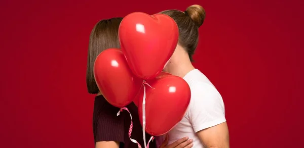 ハート型の赤い背景の上に風船をバレンタインの日のカップル — ストック写真