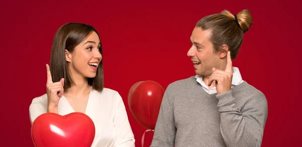 Couple in valentine day thinking an idea pointing the finger up over red background