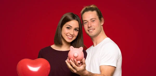 バレンタインデー赤い背景上 Piggybank を保持してのカップル — ストック写真