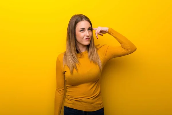 黄色の背景を頭の上に指を置き狂気のジェスチャーを作る若い女性 — ストック写真