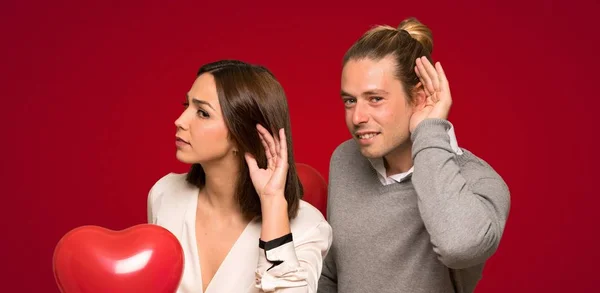 Para Walentynki Słuchając Coś Poprzez Umieszczenie Strony Ucho Czerwonym Tle — Zdjęcie stockowe