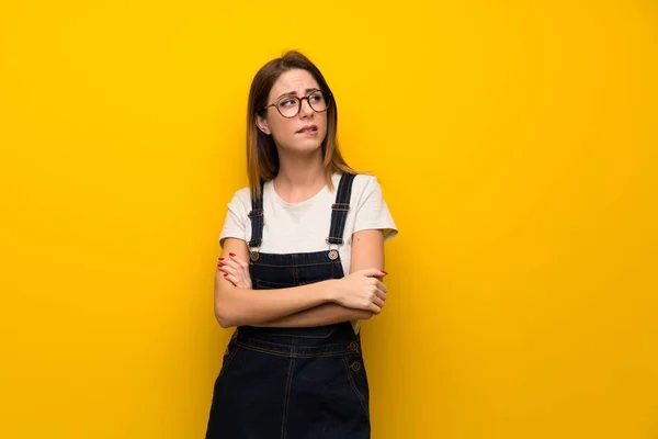 Woman over yellow wall with confuse face expression while bites lip