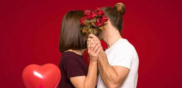 花と赤い背景上のキスのバレンタインの日のカップル — ストック写真