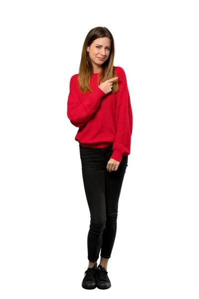 分離の白い背景の上に製品を提示する側を指している赤いセーターを持つ若い女性のフルレングス ショット — ストック写真