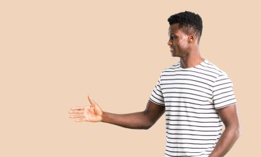 Çizgili gömlekli izole koyu sarı arka plan üzerinde iyi bir anlaşma kapanış tokalaşırken koyu tenli adam