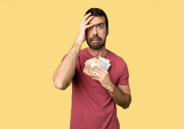 Adam bir sürü para sürpriz ve şok yüz ifadesi ile izole Sarı zemin üzerine alarak