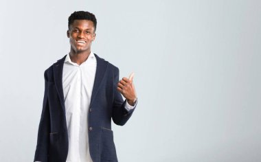 Bakarken bir ürün ya da bir fikir sunmak için yan bir parmakla işaret eden bir ceket Afro-Amerikan yakışıklı ileri üzerinde gülümseyen izole gri arka plan