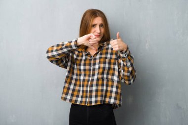 İyi-kötü işaret yapma grunge duvarın üzerinden genç Kızıl saçlı kız. Arasında kararsız Evet ya da değil