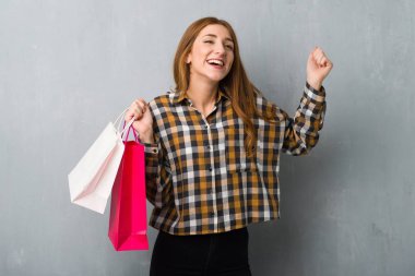 Bir sürü alışveriş torbaları zafer pozisyonlarını grunge duvarın üzerinden genç Kızıl saçlı kız