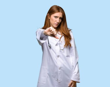 Kızıl saçlı doktor kadın başparmak aşağı işareti ile negatif ifade izole mavi arka plan üzerinde gösterilen