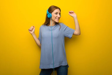 Genç Kızıl saçlı kız kulaklık ile müzik ve dans sarı duvar arka plan üzerinde