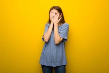 Genç Kızıl saçlı kız gözleri eller tarafından kapsayan ve parmaklarının arasından seyir sarı duvar arka plan üzerinde