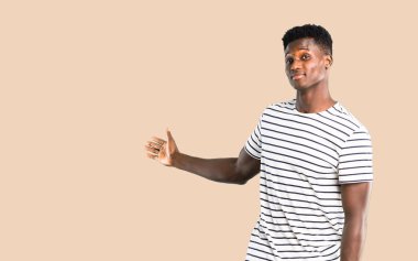 Çizgili gömlekli geri izole koyu sarı arka plan üzerinde bir ürün sunan işaret parmağı ile işaret ile adam koyu tenli