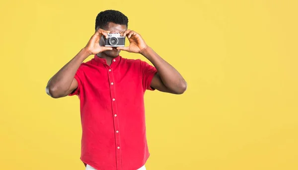 Mladý Americký Muž Držení Fotoaparátu Focení Něco Žlutém Podkladu — Stock fotografie