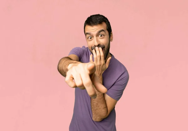 英俊的人用手指指着某人和笑在孤立的粉红色的背景 — 图库照片