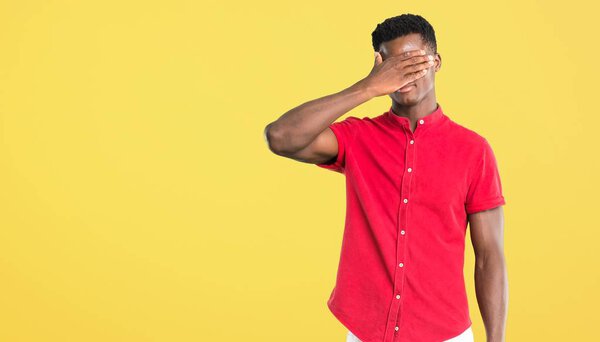 Young african american man covering eyes by hands. Do not want to see something on yellow background