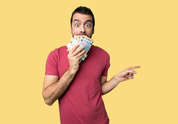 Muž Hodně Peněz Ukazováčkem Stranu Překvapený Obličej Izolované Žluté Pozadí — Stock fotografie