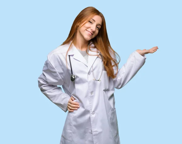 红发医生妇女拿着模仿空间想象在手掌插入广告在孤立的蓝色背景 — 图库照片