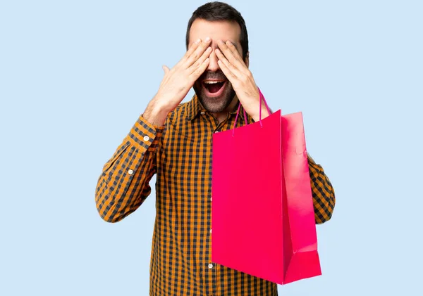 手で目を覆っているショッピング バッグを持つ男 分離された青い背景は先を見てびっくり — ストック写真