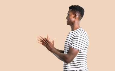 Çizgili gömlek gülümseyen ve izole koyu sarı arka plan üzerinde alkış ile koyu tenli adam