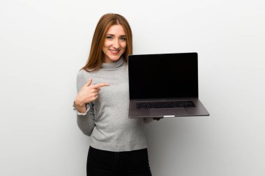 Kızıl saçlı kız dizüstü bilgisayarı gösteren beyaz duvar üzerinde