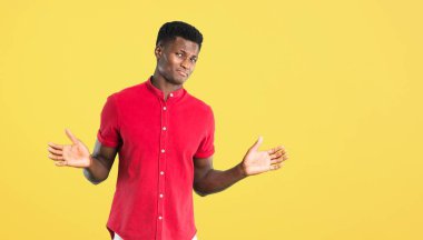 Afro-Amerikan delikanlı şüpheleri ve karıştırmayın yüzü ile yükseltme sırasında ifade eller ve Sarı zemin üzerine belirsiz kavram omuzlar