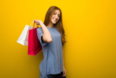 Sarı duvar arka plan alışveriş torbaları bir sürü tutan genç Kızıl saçlı kız