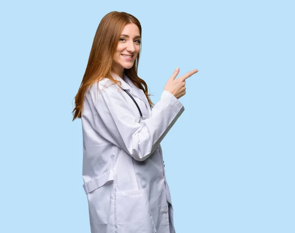 红发医生妇女指向手指在侧面位置在被隔绝的蓝色背景 — 图库照片
