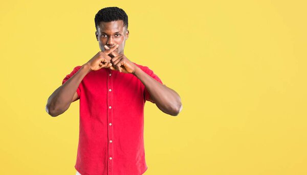 Young african american man showing a sign of closing mouth and silence gesture on yellow background